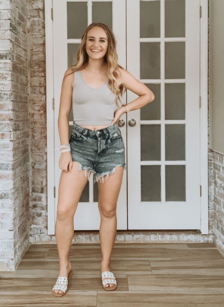 Model wearing a cropped tank top and distressed jean shorts